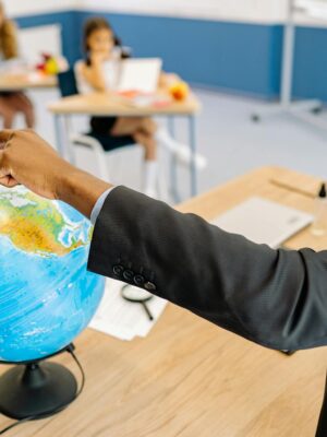 A teacher points to a globe in a classroom, engaging students in a geography lesson.