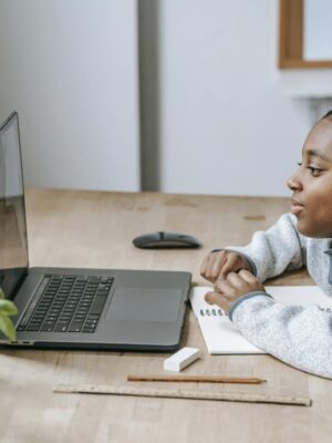 Side view of African American boy watching educational video with netbook while sitting at table with stationery